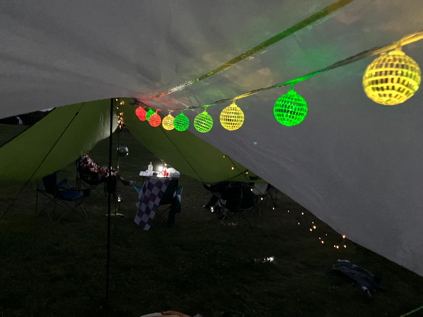 Colourful string lights hanging under camping tarp at night campsite setup
