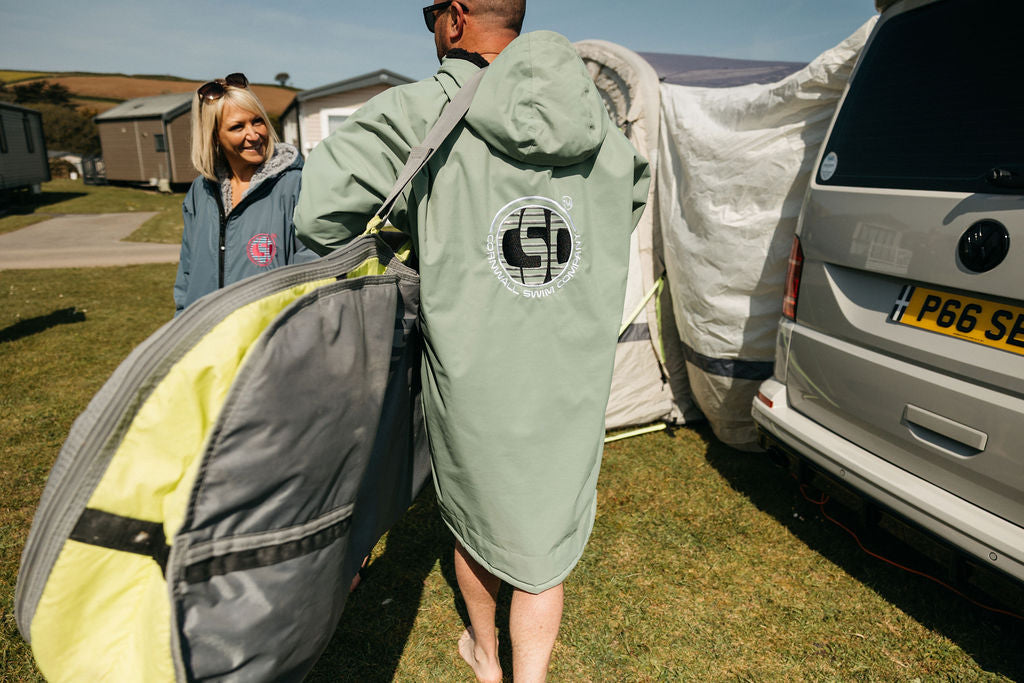 People carrying camping gear beside a caravan at campsite