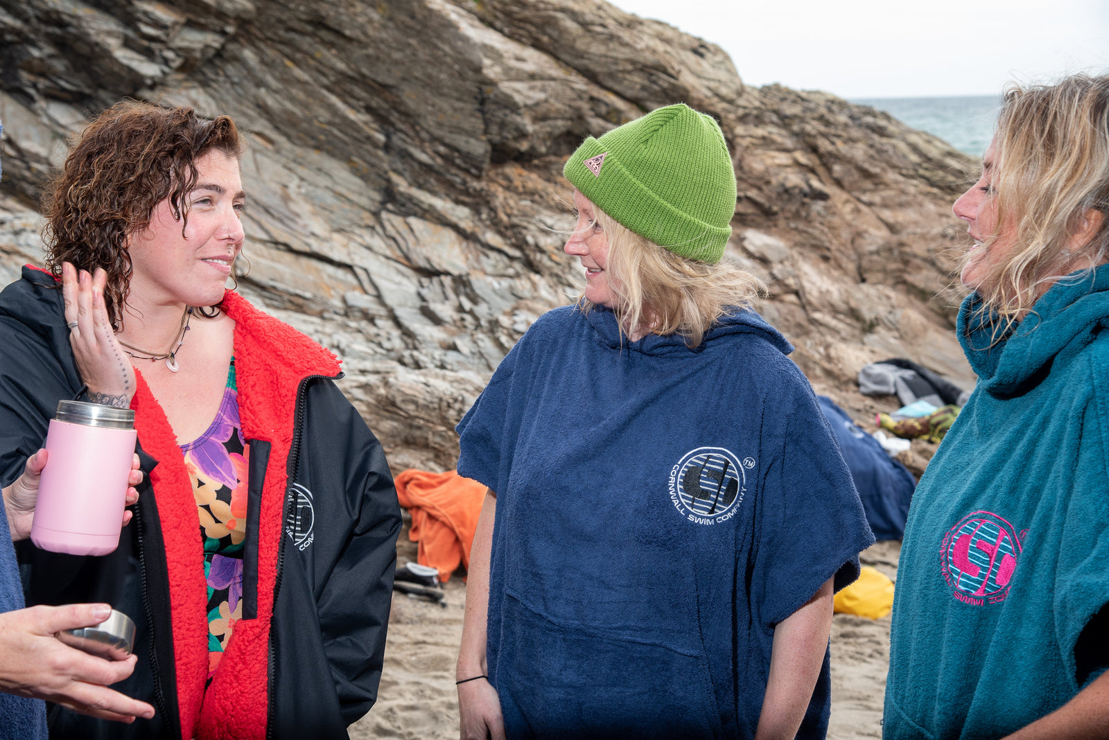 Women in changing robes socialising after sea swim on rocky beach